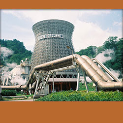 geothermal power plant surrounded by steam and large pipes in foreground