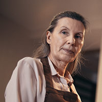 headshot of middle-aged woman in apron looking down at camera
